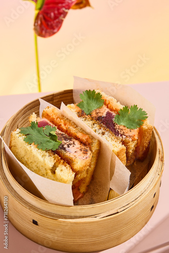 Asian sando sandwich with tuna and spicy sauce, presented in a bamboo steamer amidst abstract floral art photo