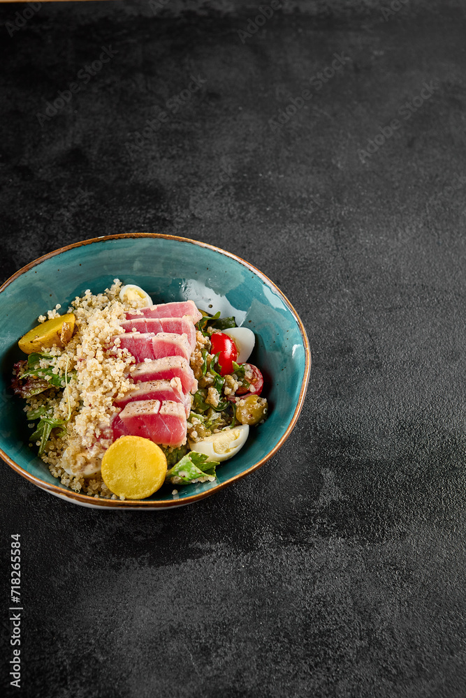 A quinoa bowl topped with medium-seared tuna slices, garnished with vegetables, in a turquoise ceramic dish