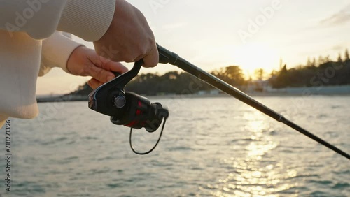 Reel of fishing rod hand rotation of orange sunset slow motion. Woman hobby fishing on sea tightens fishing line reel fish summer. Lens flare. Calm surface sea. Bright disk of sun Go Everywhere photo