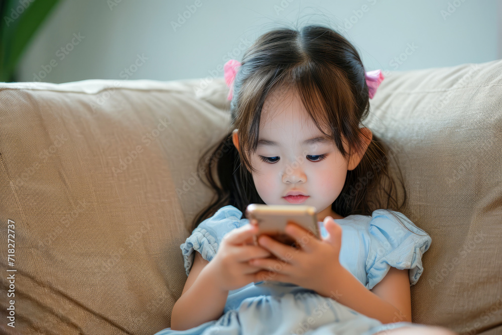 Asian child sitting on a sofa, browsing internet on mobile device and playing with smartphone apps