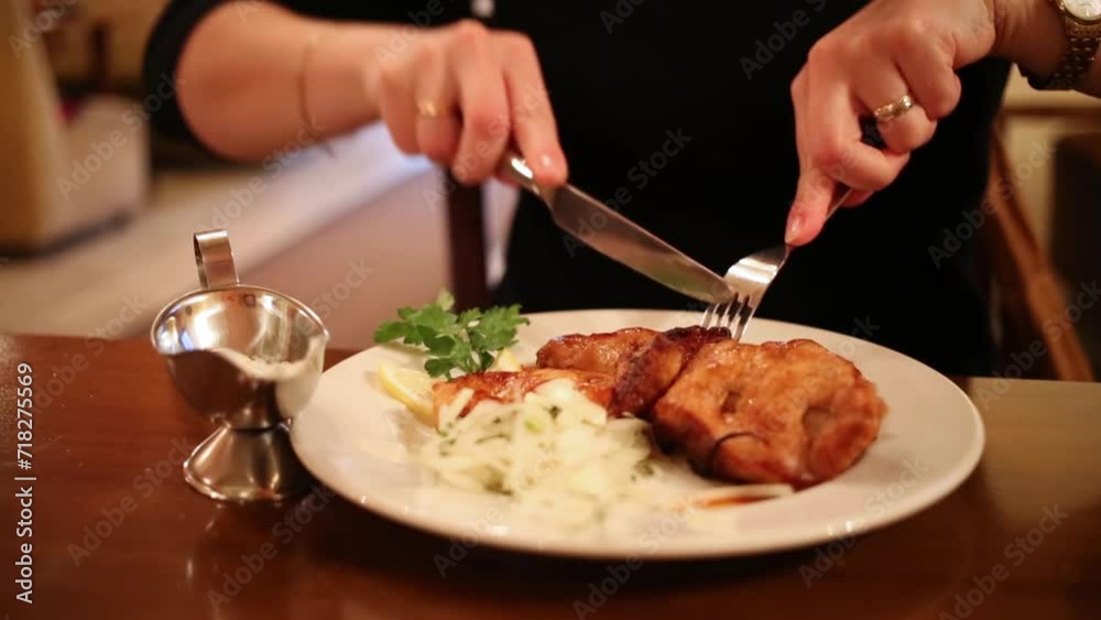 Close up of hand with knife and fork cutting meat in dish on table. Close up of hand with knife and fork cutting meat in dish on table.