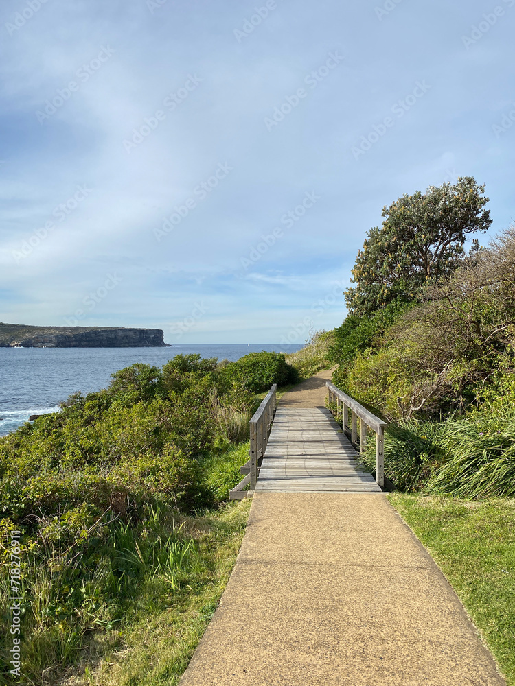 Coastal landscape with a wooden bridge near the blue ocean. Walkway to the beach. Path next to the sea. 
