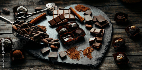 Four handmade chocolate candies on blackstone stand. Closeup chocolate candies with cocoa beans, nuts around