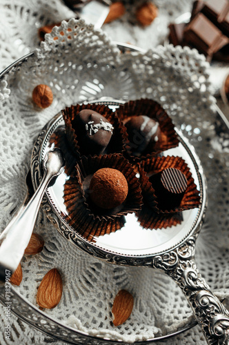 Four handmade chocolate candies on silverplated plate. Closeup chocolate candies with almond nuts around