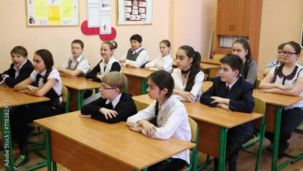 Thirteen children sitting at their desks, some of them raise their hands Thirteen children sitting at their desks, some of them raise their hands