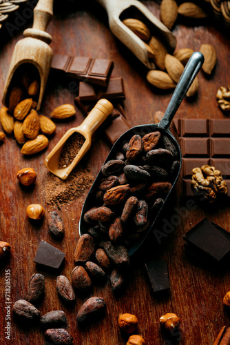 Metal scoop with cocoa beens beside with chocolate nuts, cacao beans on on wood stand. Top view.