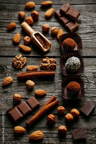 Handmade candies, two truffles with cocoa powder and one with coconut flakes. Chocolate candies inside of candy wrapper on wood table stand with nuts