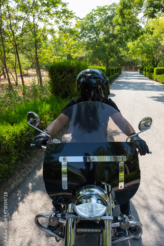 Helmet and tattooed biker riding motorcycle on forest road