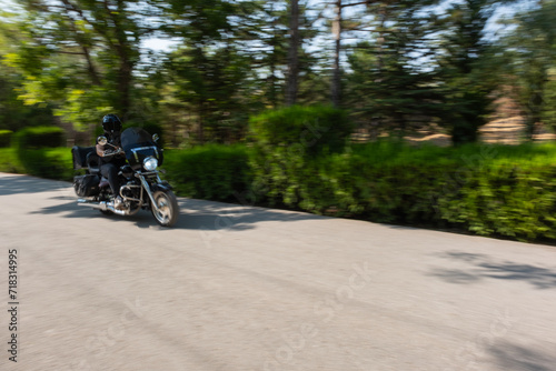 Helmet and tattooed biker riding motorcycle on forest road