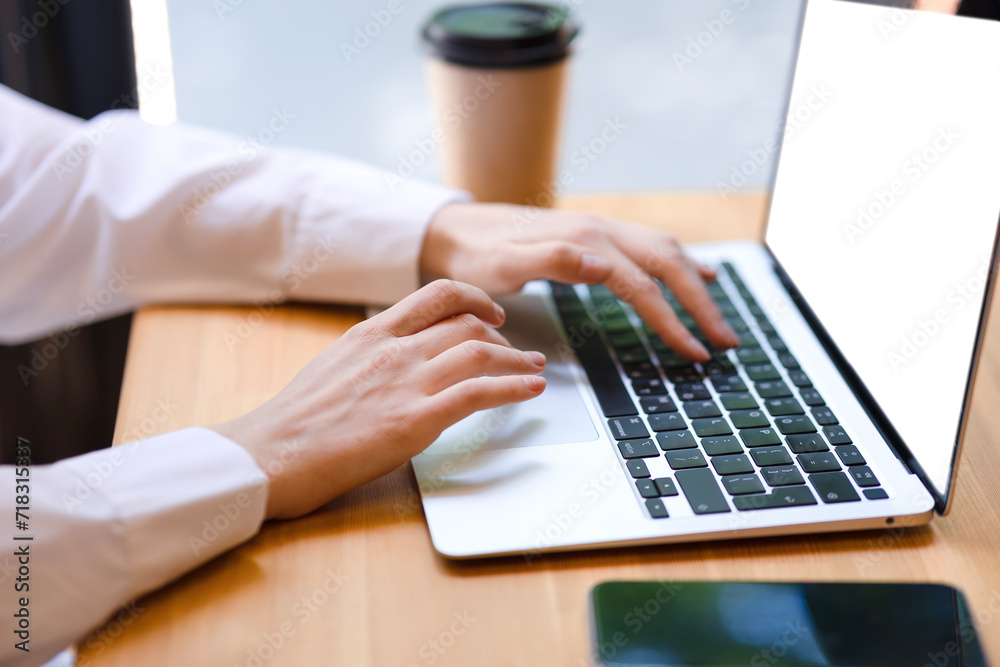 Female hands in white office shirt close-up typing on laptop. Woman working on laptop in office, girl writing notes, on wooden table laptop with white screen, phone, glass Female hands in white office shirt close-up typing on laptop. Woman working on laptop in office, girl writing notes, on wooden table laptop with white screen, phone, glass