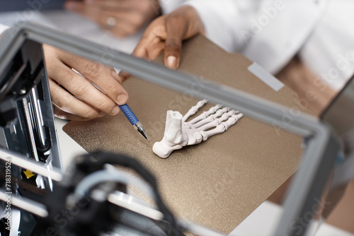 Close up shot of unrecognizable technicians hand pointing pen at calcaneus of printed 3D foot bone on aluminum print bed photo