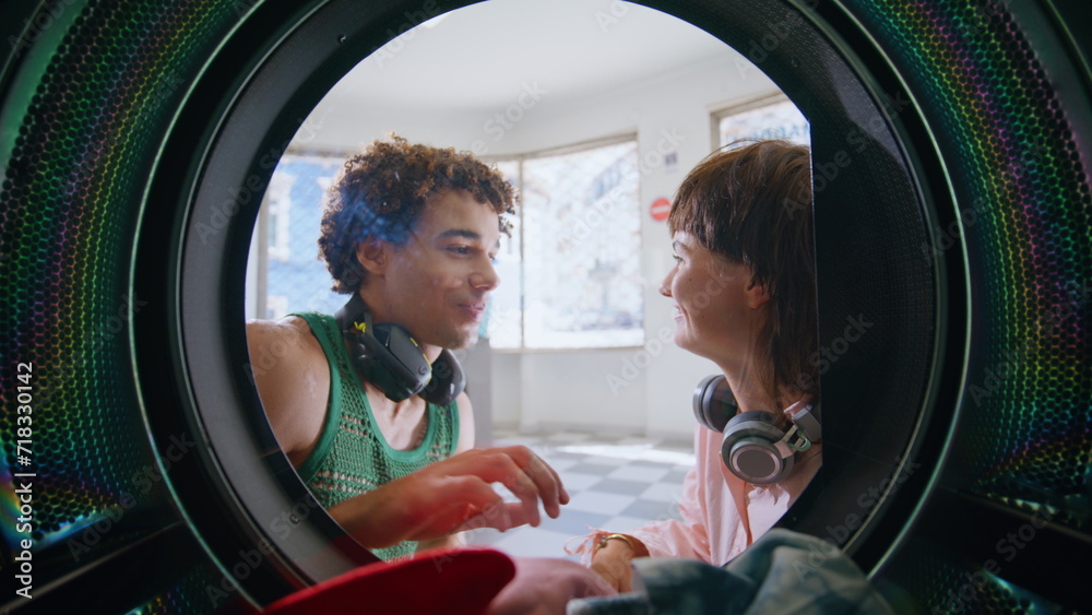 Couple talking public laundromat closeup. Smiling friends wait in laundry room - obrazy, fototapety, plakaty 