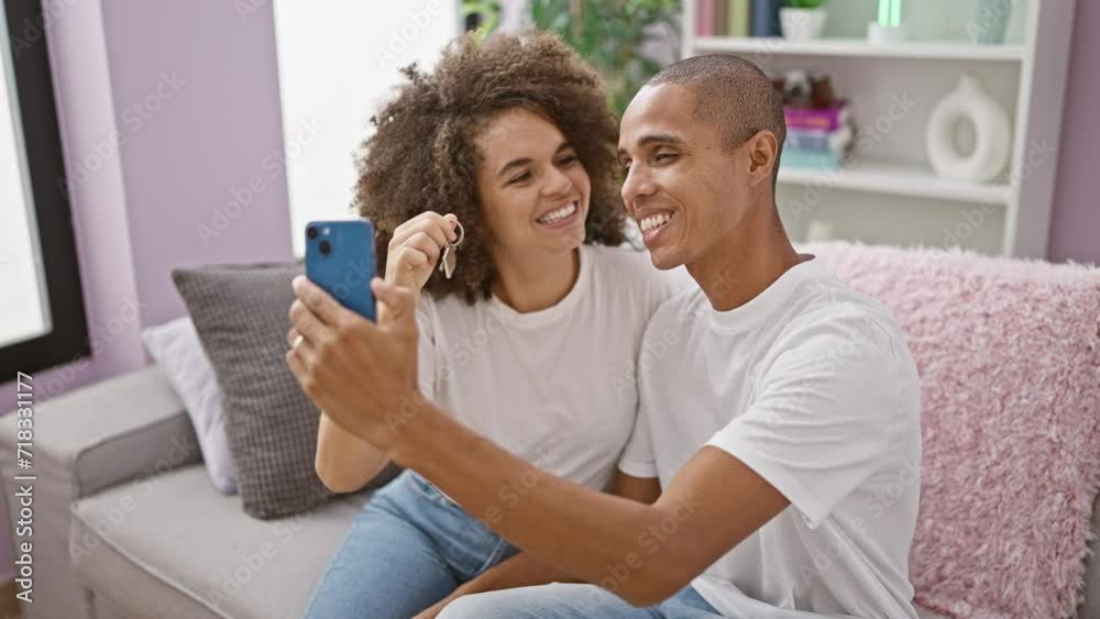 Smiling beautiful couple holding key, enjoying a video call at their new home, excitedly sharing their milestone of buying property together, sitting comfortably in the living room Smiling beautiful couple holding key, enjoying a video call at their new home, excitedly sharing their milestone of buying property together, sitting comfortably in the living room