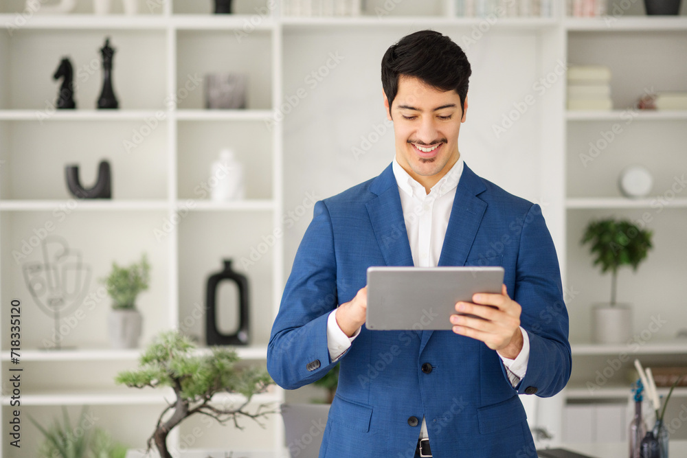A cheerful Hispanic businessman interacts with a tablet, with a look of satisfaction, in a well-organized office, concept of digital tools for business efficiency A cheerful Hispanic businessman interacts with a tablet, with a look of satisfaction, in a well-organized office, concept of digital tools for business efficiency