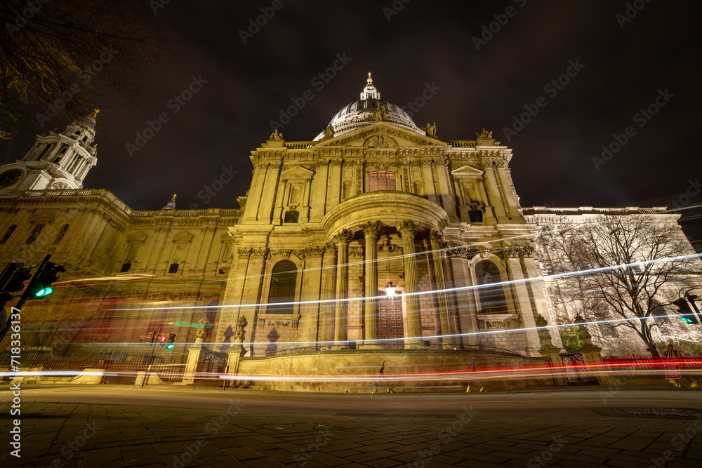 A street view of the facade of St. Paul's Cathedral at night time with light trails from passing vehicles.