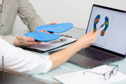 Doctor consulting male patient on custom orthotic insoles in a clinic for a personalised custom fitusing test picture on a laptop.