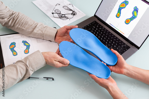 Female doctor orthopedist  presents new custom made insoles to a male patient in a clinic. photo