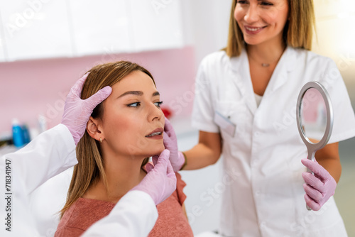 A doctor examines the patient before the aesthetic procedures. The patient looks at herself and tells her what she wants to change.