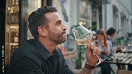 Bearded guy tasting wineglass open air restaurant closeup. Man enjoying alcohol photo