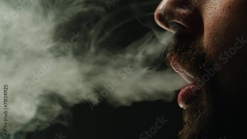 Young man smoking hookah or cigarette on black background close-up. Smoke, vapour and fog texture. photo