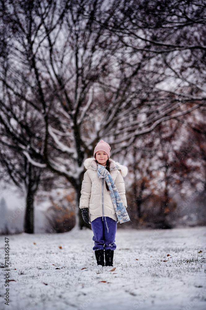a young girl standing in a snowy landscape, with a backdrop of leafless trees, wearing a winter coat, a pink beanie, and a scarf a young girl standing in a snowy landscape, with a backdrop of leafless trees, wearing a winter coat, a pink beanie, and a scarf