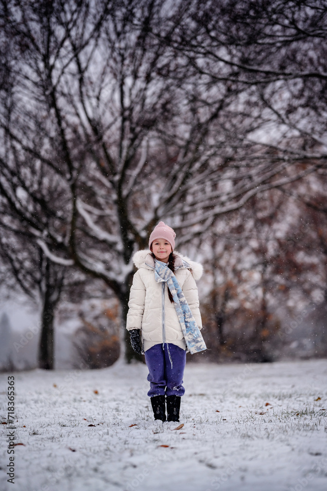 A young girl standing in a snowy landscape, with a backdrop of leafless trees, wearing a winter coat, a pink beanie, and a scarf A young girl standing in a snowy landscape, with a backdrop of leafless trees, wearing a winter coat, a pink beanie, and a scarf