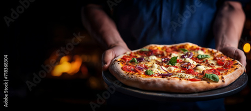 Delicious freshly baked pizza with tomatoes, cheese, and basil held by chef in a restaurant with a warm ambience
