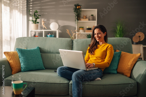 Portrait of a woman using laptop while sitting on a mint couch at home photo