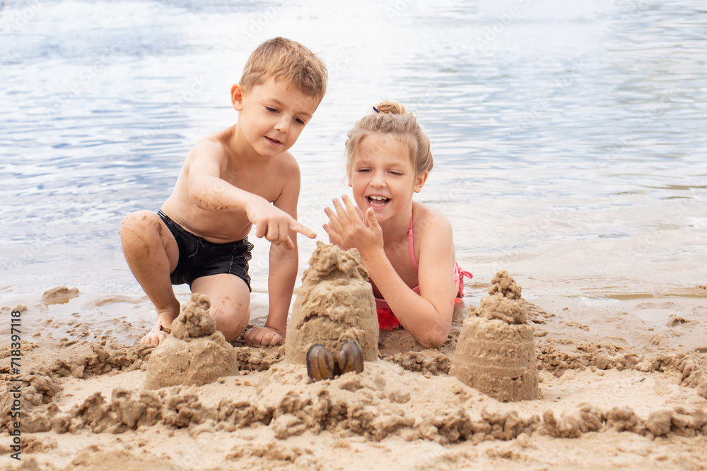 Boy and girl laughing and playing on the nice beach on summer holidays. happy children building a sandcastle at the sea Boy and girl laughing and playing on the nice beach on summer holidays. happy children building a sandcastle at the sea