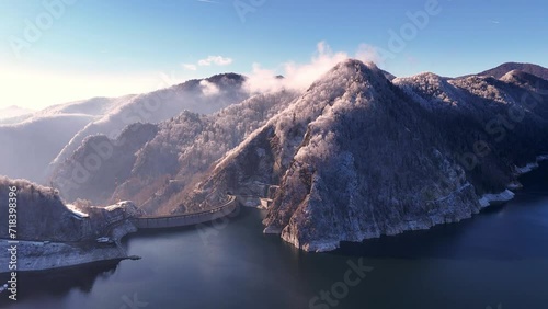 Aerial view of Water dam between snow covered mountains. Reservoir between high mountains. Hydroelectric power plant. Frozen trees in the mountain forest. Vidraru Reservoir in the Fagaras.   photo