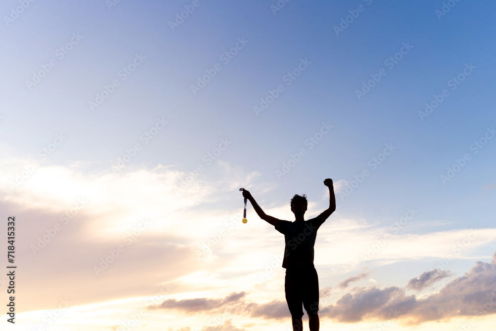 Silhouette of an athlete celebrating the gold medal against a sunset sky adorned with golden clouds in the background. Ideal for conveying the spirit of success in sporting events.