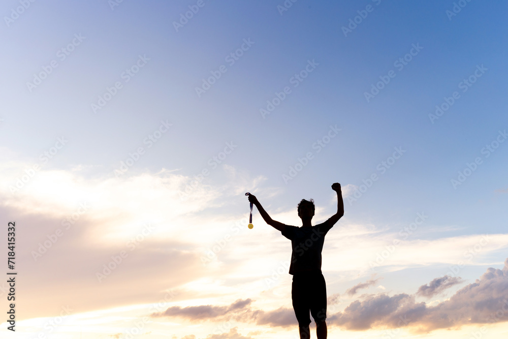 Silhouette of an athlete celebrating the gold medal against a sunset sky adorned with golden clouds in the background. Ideal for conveying the spirit of success in sporting events. Silhouette of an athlete celebrating the gold medal against a sunset sky adorned with golden clouds in the background. Ideal for conveying the spirit of success in sporting events.