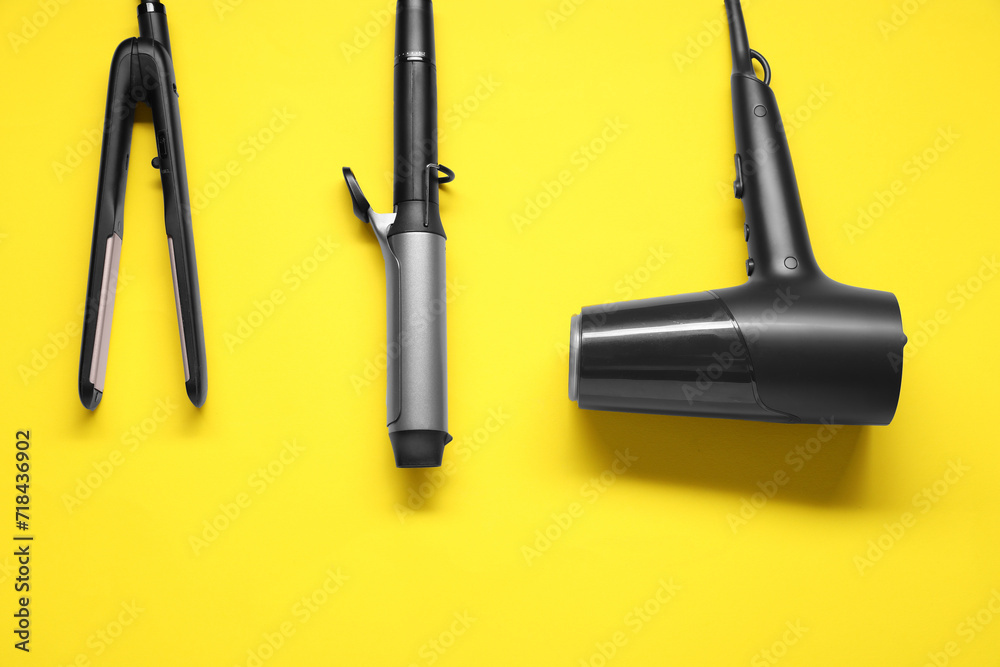 Curling iron, hair straightener and dryer on yellow background, flat lay Curling iron, hair straightener and dryer on yellow background, flat lay