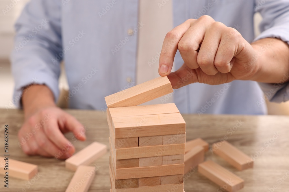 Playing Jenga. Man building tower with wooden blocks at table, closeup Playing Jenga. Man building tower with wooden blocks at table, closeup