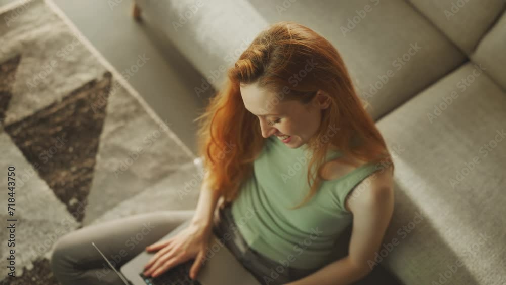 Attractive long haired woman working online from home on laptop while sitting on floor in the living room, top view