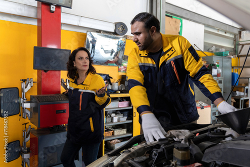 Professional Uniformed Car Mechanic Working in Service Station. Team Discussing and Repairing Vehicle. Car's Engine in The Uniform Works in The Automobile Selective Focus