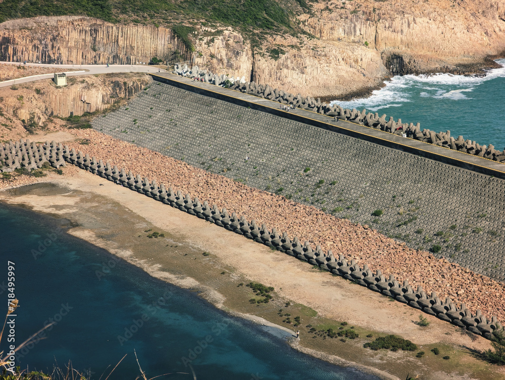  A large dam with tetrapod wave breakers, surrounded by a rocky landscape and the sea. 