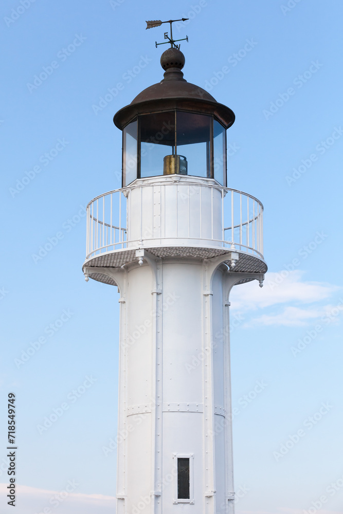 White lighthouse tower with black roof and vane is under blue sky on a daytime