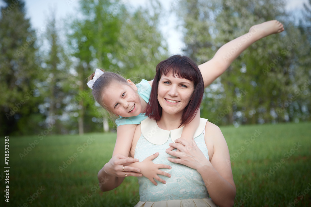 Happy mother and daughter enjoying rest, playing and fun on nature on a green lawn and with a blooming apple tree in the background. Woman and girl resting outdoors in summer and spring day Happy mother and daughter enjoying rest, playing and fun on nature on a green lawn and with a blooming apple tree in the background. Woman and girl resting outdoors in summer and spring day