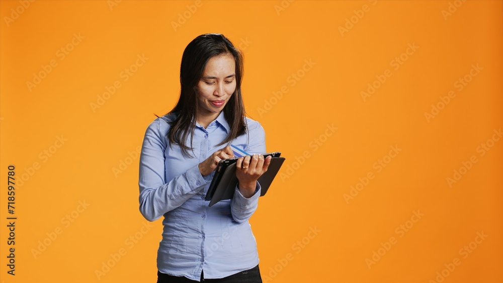 Asian model buying clothes on internet using tablet, typing credit card information on website for online shopping spree. Pretty woman in casual attire purchasing things on device. Asian model buying clothes on internet using tablet, typing credit card information on website for online shopping spree. Pretty woman in casual attire purchasing things on device.