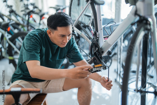 handsome young man installing bicycle pedals with allens key in bicycle shop