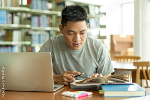 male asian student studying and reading book in library photo