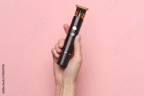 Hand holding hair trimmer on pink background