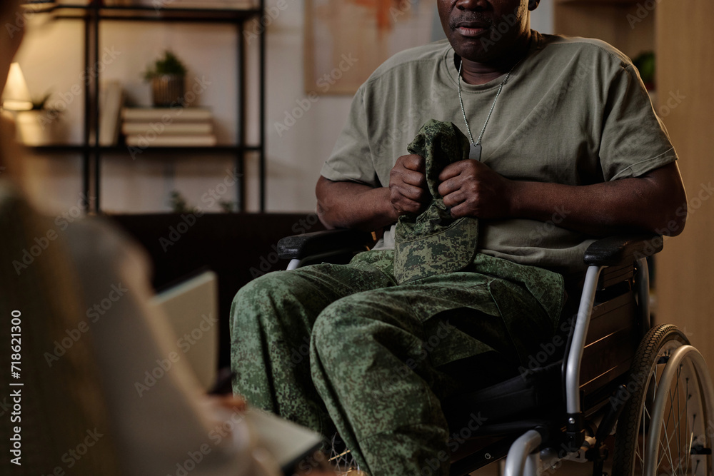 Fototapeta premium Black war veteran with PTSD firmly holding his uniform headwear at session with psychologist