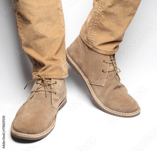 Male legs in beige pants and suede desert shoes on a white background