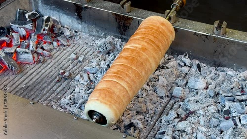 Unrecognizable person taking chimney cake with golden crisp from grill, close up of rotating underbaked pastry on a baking dowel, tubular treats of Hungary. High quality 4k footage photo