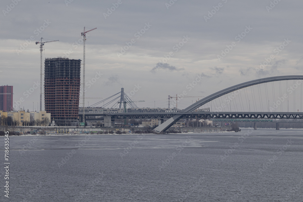 Fototapeta premium Kyiv, Ukraine - January 19, 2024: it's cold outside, minus temperature, gray sky. the Dnipro River froze over. From a height you can see the beautiful architecture near the embankment and on Podil