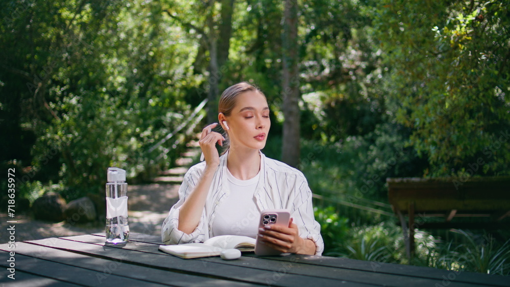 Happy woman headphones answering video call at smartphone on park table close up