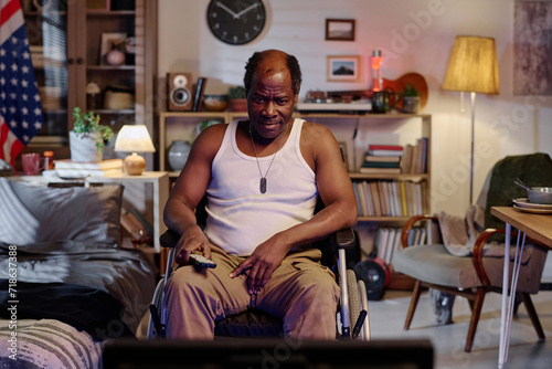Smiling african american man in wheelchair sitting in front of TV in his bedroom watching program
