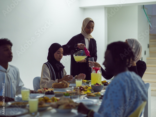 A diverse Islamic family gathers for iftar, joyfully breaking their fast together during Ramadan, with a Muslim woman in a beautiful hijab gracefully pouring water to mark the end of their fast